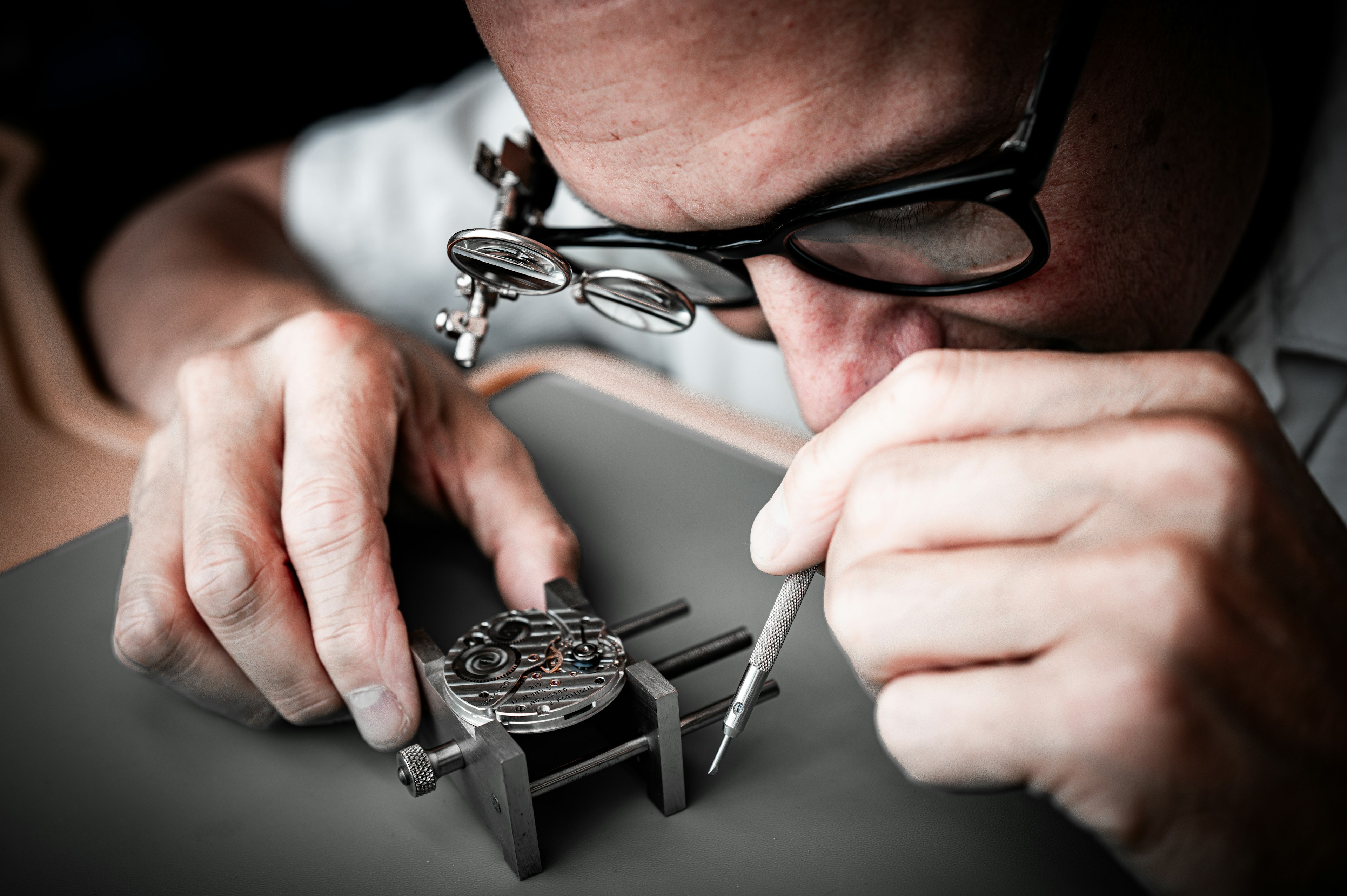 A watchmaker examining a mechanical movement with a loupe — expert watch and jewelry services at Saleh Jewelers